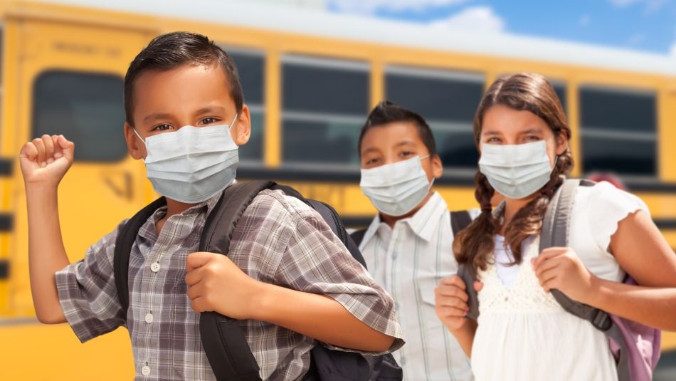 Students wearing masks and backpacks standing in front of a school bus
