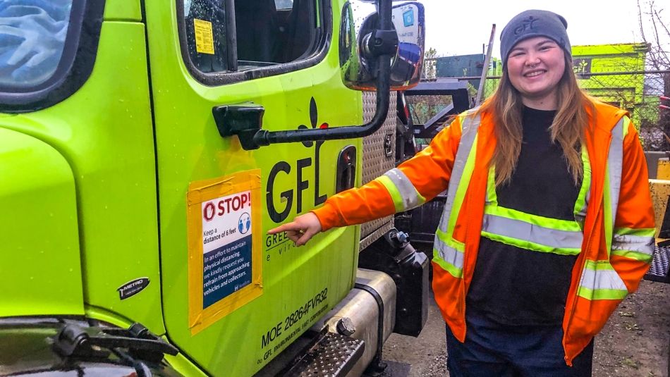 Waste vehicle operator in hi-vis gear smiling and pointing to their green truck