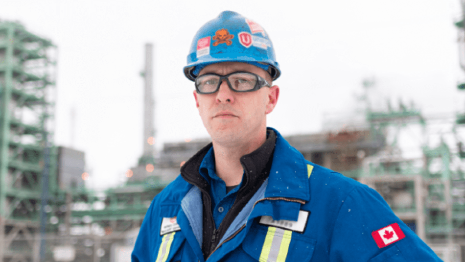 worker in overalls and hard hat standing outside of a refinery