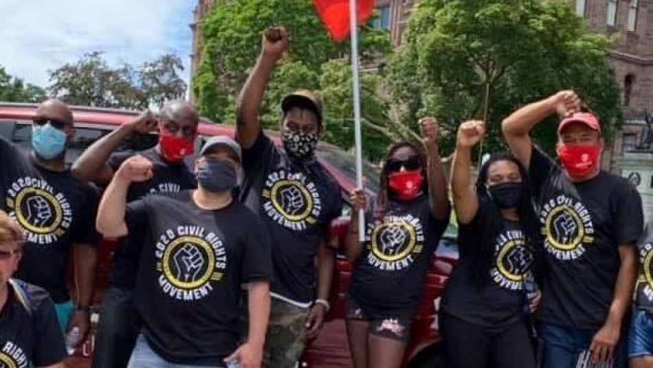 Christine Maclin et un groupe diversifié de militantes et militants d'Unifor portant des t-shirts assortis pour la justice raciale lèvent le poing en signe de solidarité.