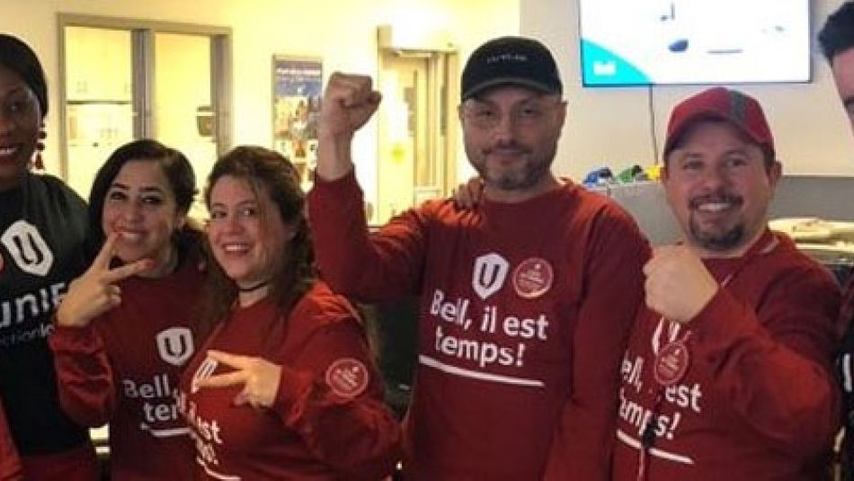 A diverse group of Unifor members, in matching Unifor shirts, raise their fists in solidarity.