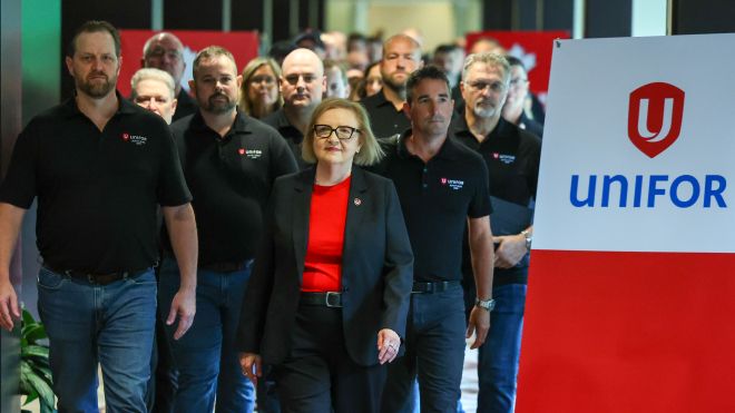 people walking down a hallway near a Unifor sign 