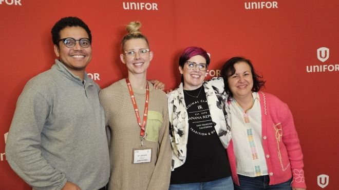 Four people posing in front of a Unifor banner