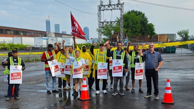 A group of people outside in the rain holding "On Strike" placcards