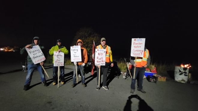 Five people on a picket line at night holding placards