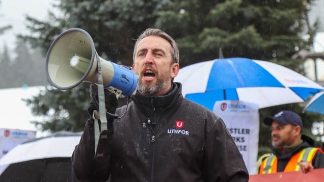 Gavin McGarrigle speaking into a megaphone in front of a crowd holding umbrellas.