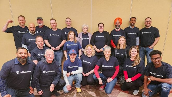 Group of Unifor member organizers wearing black UniforVotes tees posing for a photo, one row standing, one row in front kneeling.