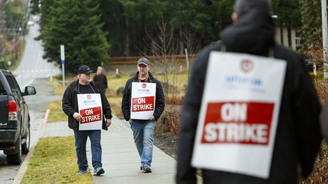 Workers wearing "on strike" placards walking on a sidewalk.