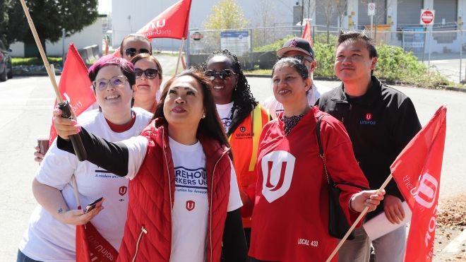 A group of people posing for a selfie wearing Unifor gear and holding Unifor flags. 