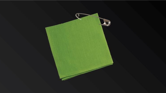 A green square of fabric with a safety pin attached in front of a black background.