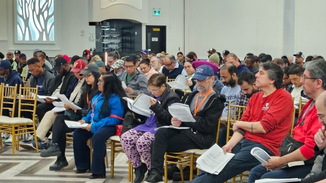 Ballroom full of people seated, many reviewing a paper document.