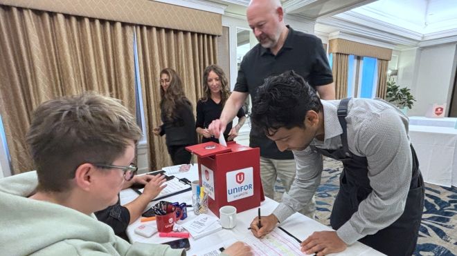 A seated person watching a standing person mark a ballot while another standing person looks on