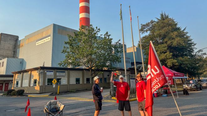 Three Local 433 members standing outside near a Unifor flag with an industrial building and striped smoke stack.