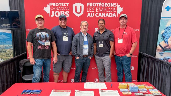 Five men standing in front of a backdrop reading 'Protect Canadian Jobs' with Unifor logos. A table is in the foreground with papers and pens.