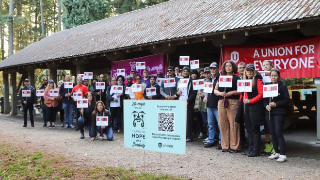 A group of two dozen members stand outdoors holding small signs behind a lawn sign reading Tears to Hope with a QR code.