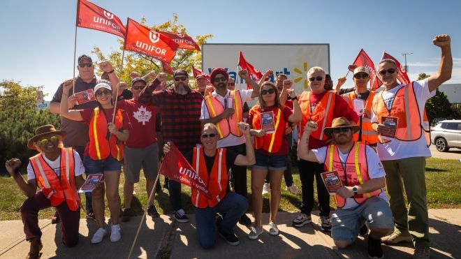 A large group holding Unifor flags wearing safey vests