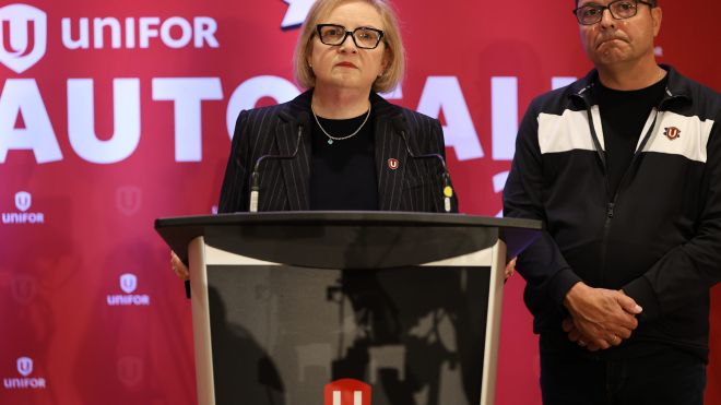 A women at a podium a man stands behind 