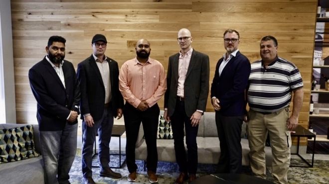 Six men standing in front of a wood plank wall.