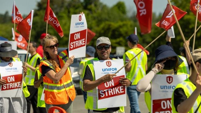 A goup wearing yellow saftey vests holding red Unifor flags