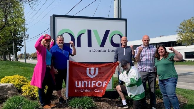 Six people holding a red Unifor flag outside an Ariva sign.