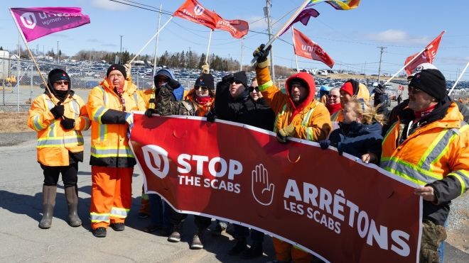 Group of workers hold an anti-scab banner and Unifor flags
