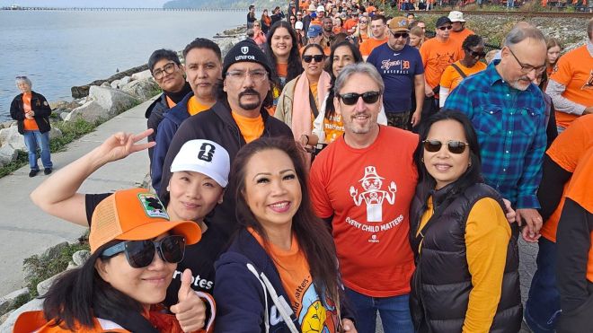 Unifor members post for a selfie in the middle of a march along the waterfront, with a long line of marchers visible behind them.