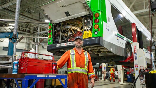 A man in orange and yellow coveralls in a bus factory 