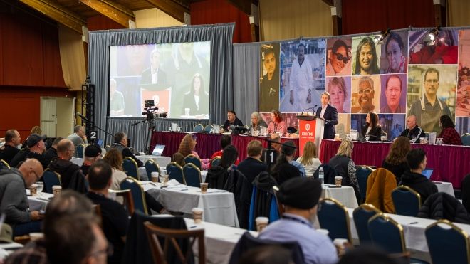 Une grande salle où les gens sont assis comme dans une salle de classe et où une personne parle depuis un podium.