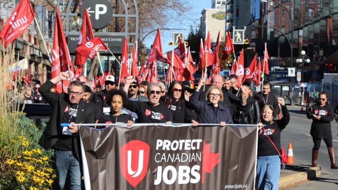 People marching with red Unifor flags and a “Protect Canadian Jobs” banner.