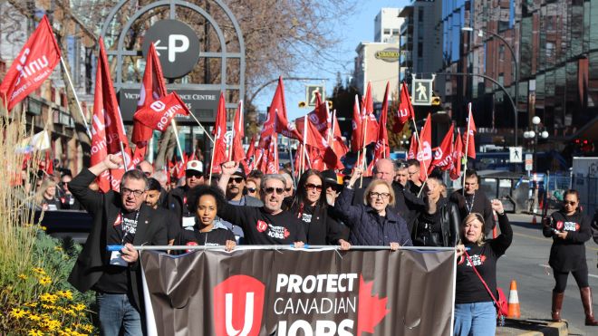 People marching with red Unifor flags and a “Protect Canadian Jobs” banner.