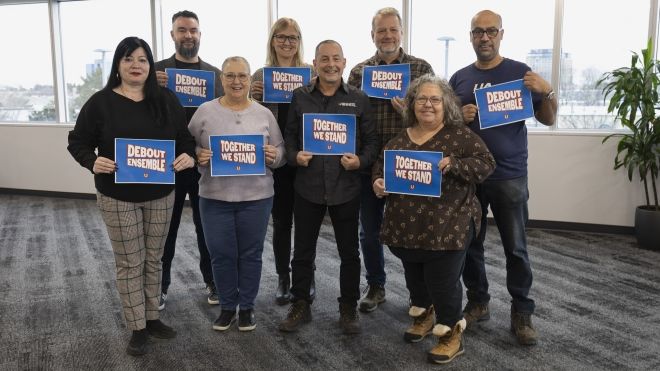 A group of people holding placcards that read; Together we stand with a Unifor logo