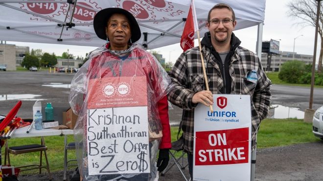 A women and a man standing in front of a tent holding place cards that read on strike