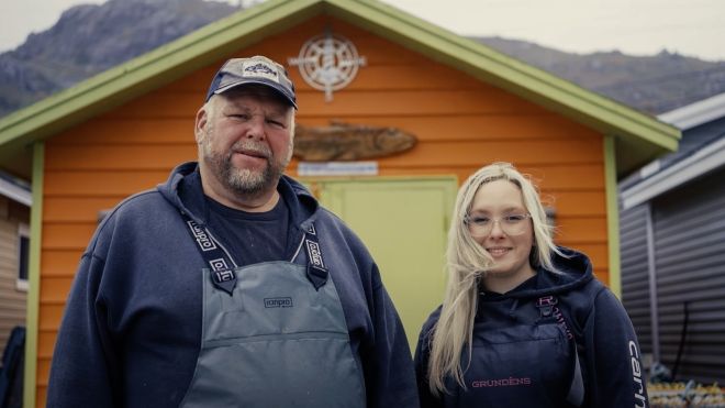 A man and women wearing coveralls in front of a fishing shead