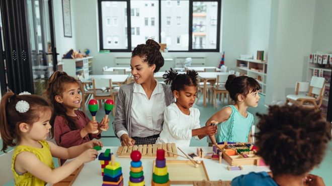 A child care worker sitting at a table with several young children playing games.