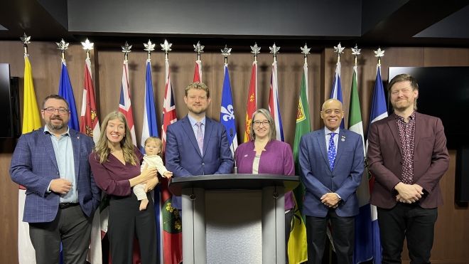 Unifor Quebec Director stands at the left-hand of a group of 7 people, with a backdrop of Canadian provincial flags.