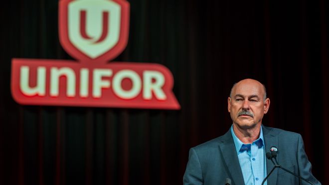 A man at a podium Unifor shield sign on a black background