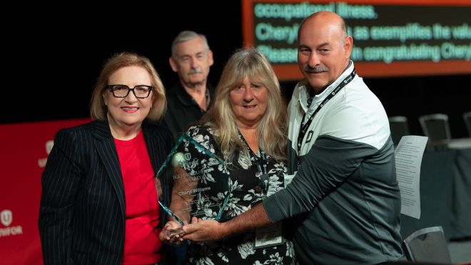 Three people on stage a women holding a glass dimond shaped award 