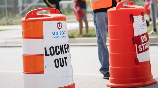 A man holding a red Unifor flag wearing a safety vest