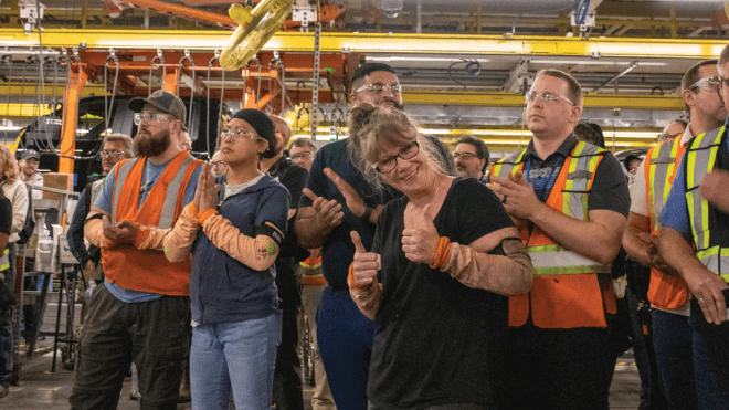 A group of workers wearing safety vests stand together with one woman giving the thumbs up. 