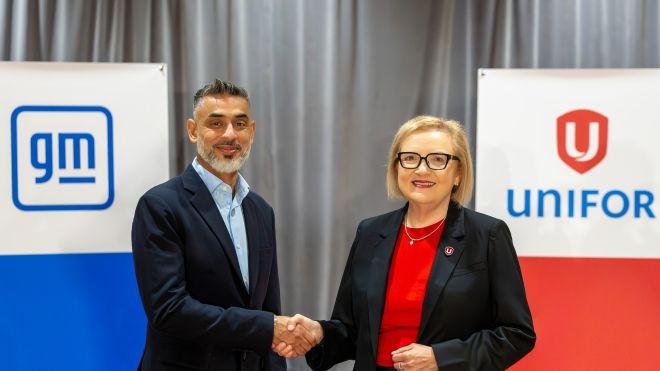 A man with a blue GM sign in the background shakes Lana's Payne's hand with a Unifor red stand behind her.