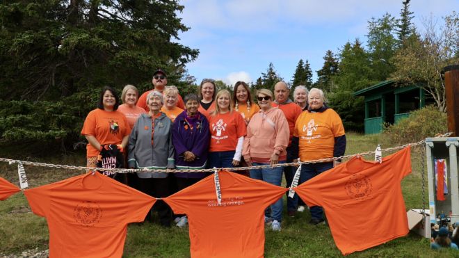a row of orange shirts strung up and a large group wearing orange shirts are in behind