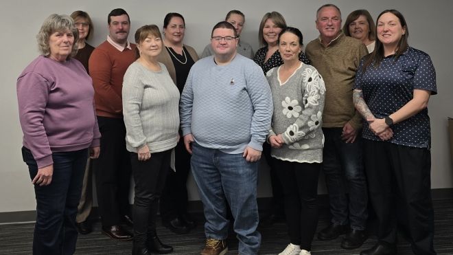 A large group smiling at the camera in front of a beige wall
