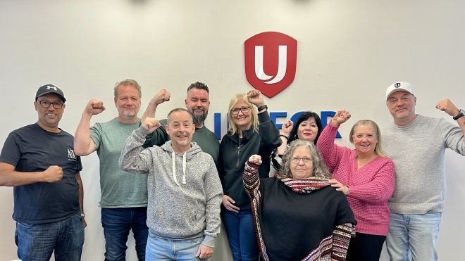 nine people stand in front of a Unifor sign fists raised.
