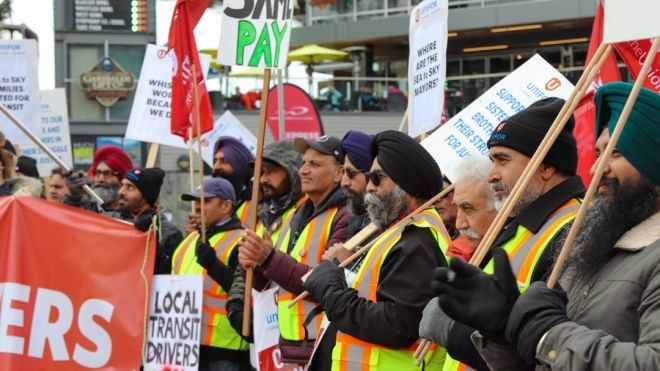Several transit workers holding flags and placards watching events at a rally.