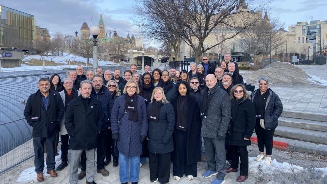 A large group outside, in dark winter coats, on a cold sunny day