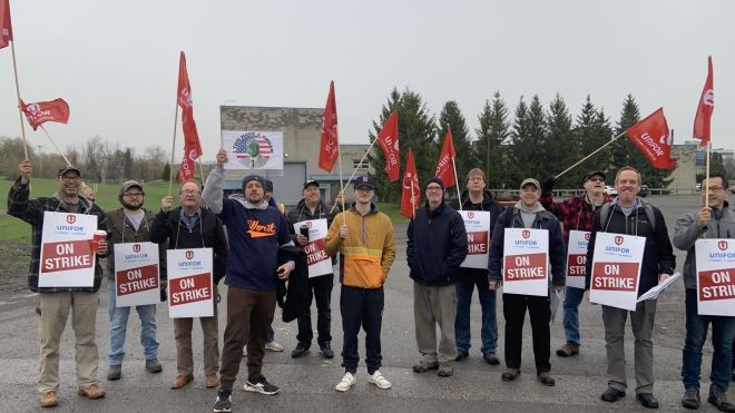 A goup of people standing holding place cards that read, on strike and Unifor flags