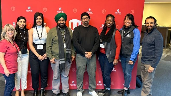 Eight delegates posing for a photo in front of a red backdrop with Unifor logos