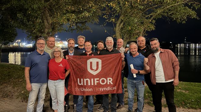 A group at night holding up a red Unifor flag