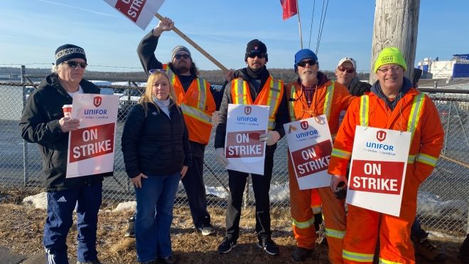 a group of striking workers stand with picket signs