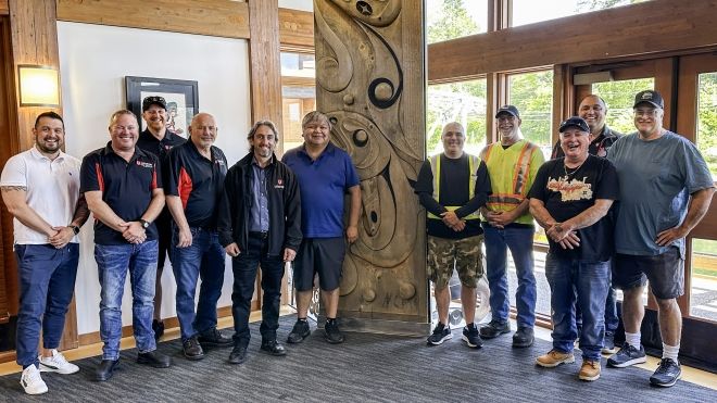 Ten people standing indoors next to a totem pole.